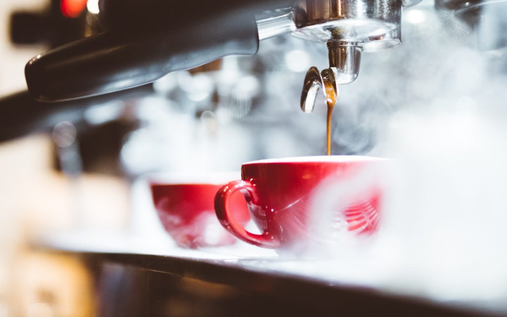 A barista brews espresso surrounded by steam.