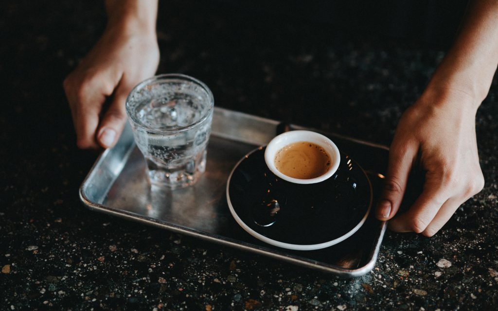A barista serves espresso with water.